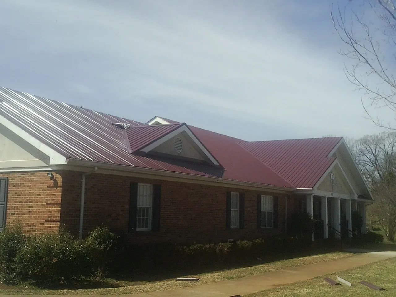 Red metal roof with gabled entries on a long brick building, from a Hail Damage Roof Repair job in Ellenburg Center