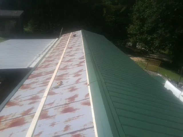 Old rusted panels beside newly installed green metal roofing — Wind Damage Roof Repair by Roofing Brothers in Ellenburg Center