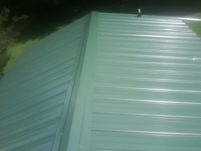 New green metal panels meeting at the ridge of a roof — Flat Roof Repair work by our crew in Ellenburg Center