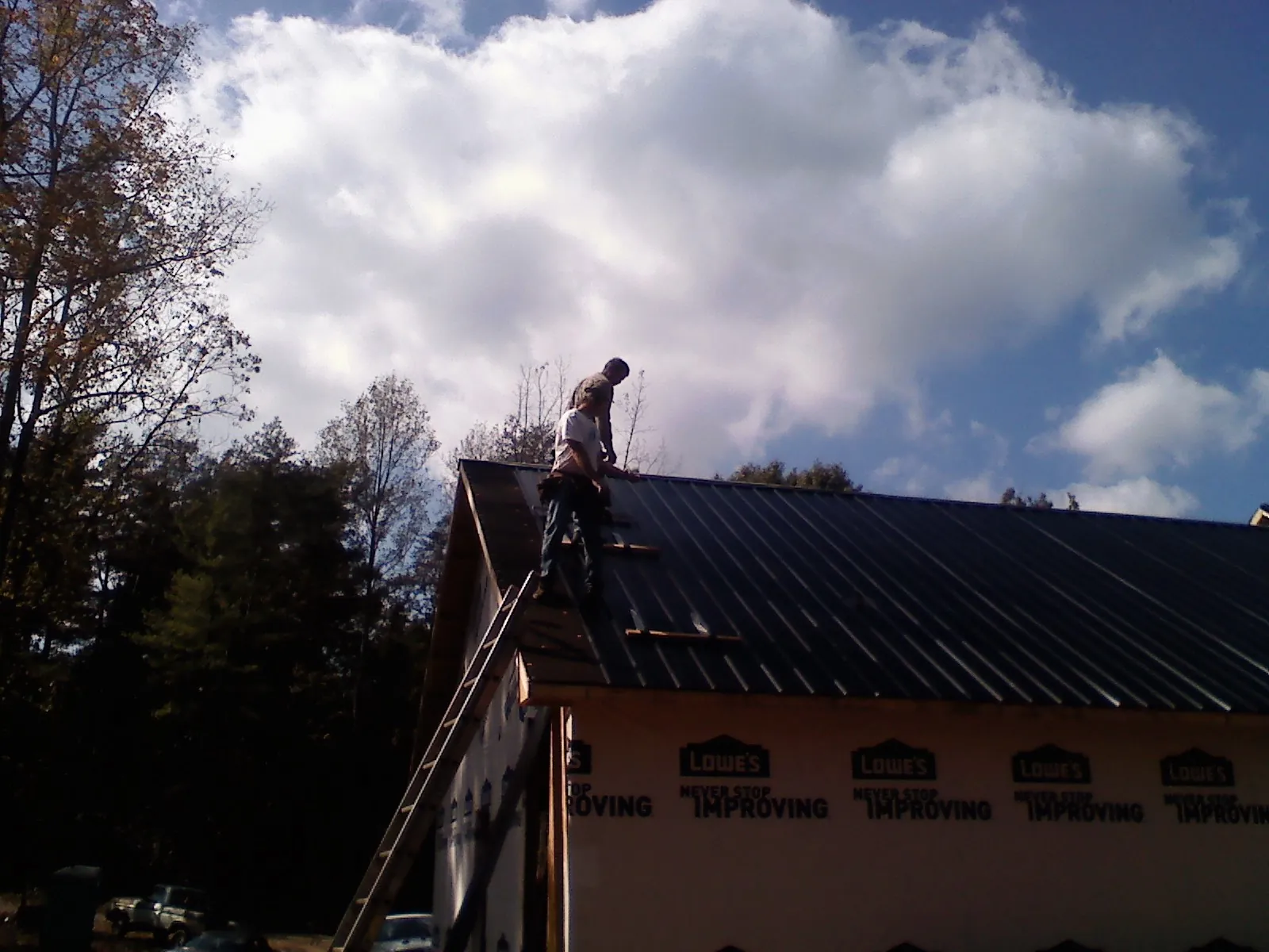 Roofer fastening dark metal panels high against a cloudy sky, from a Roof Inspection job in Ellenburg Center