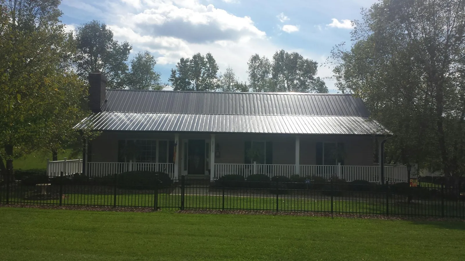 Gray metal roof on a brick ranch with a full width front porch — Gutter Guard Installation work by our crew in Ellenburg Center