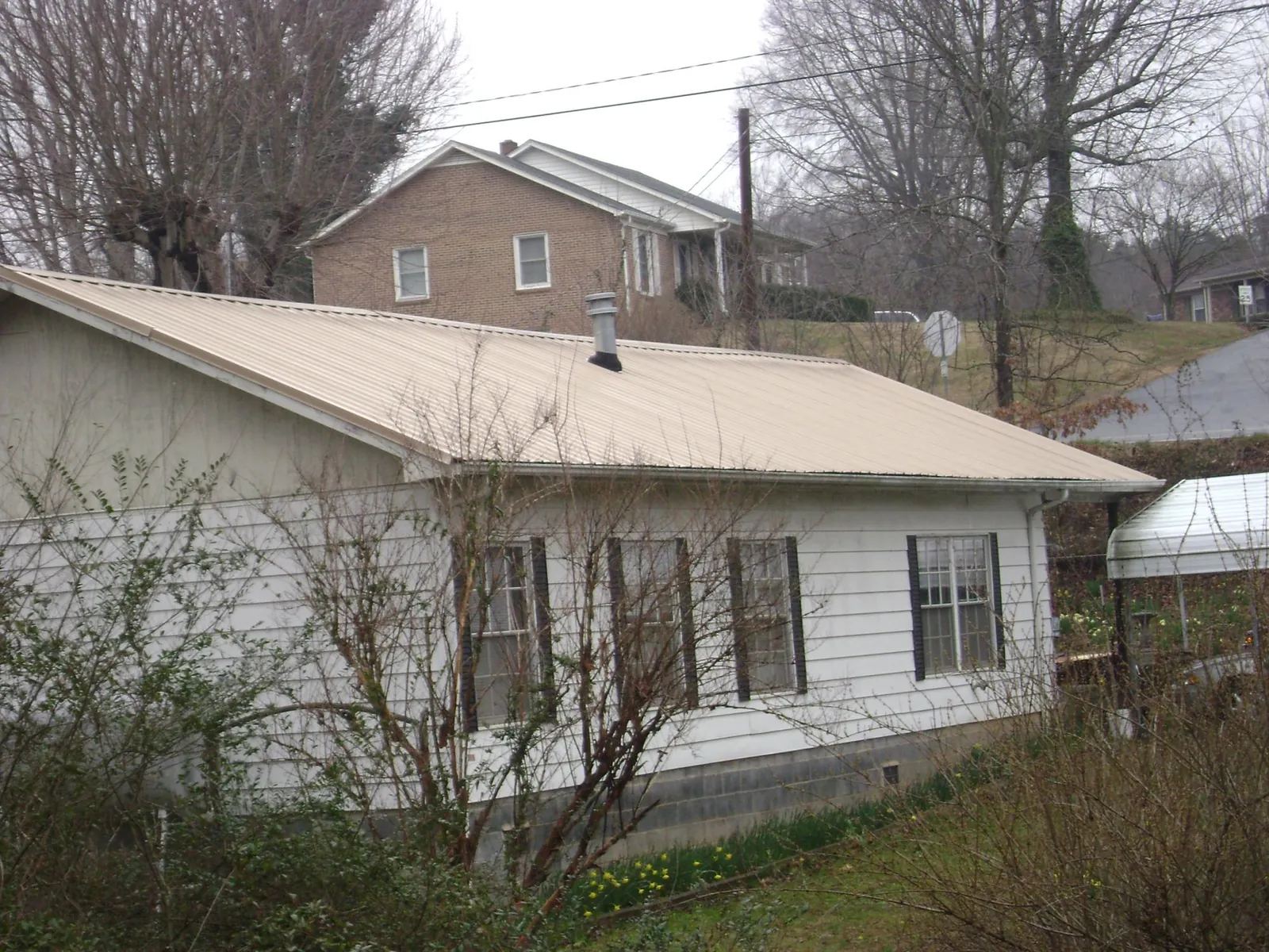 Tan metal roof on a white sided house set into a hillside — Commercial Roofing by Roofing Brothers in Ellenburg Center