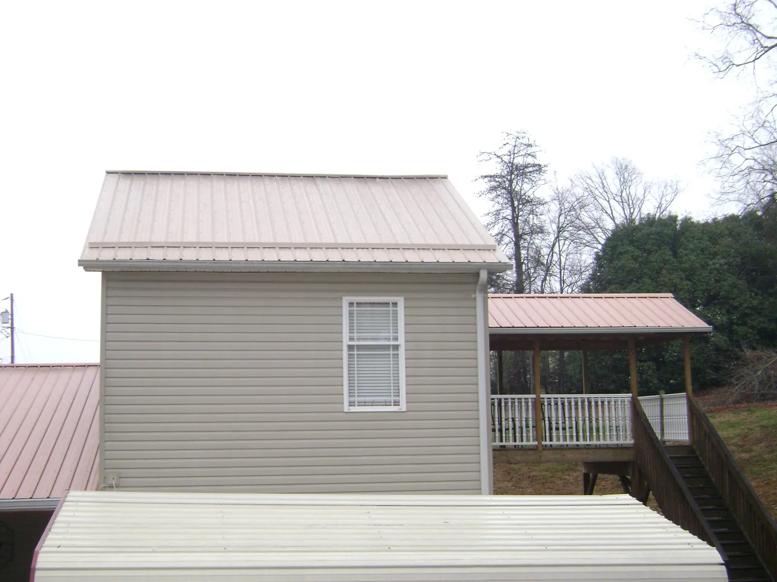 Tan metal roofs on a two story addition and attached porch, from a Roof Replacement job in Ellenburg Center