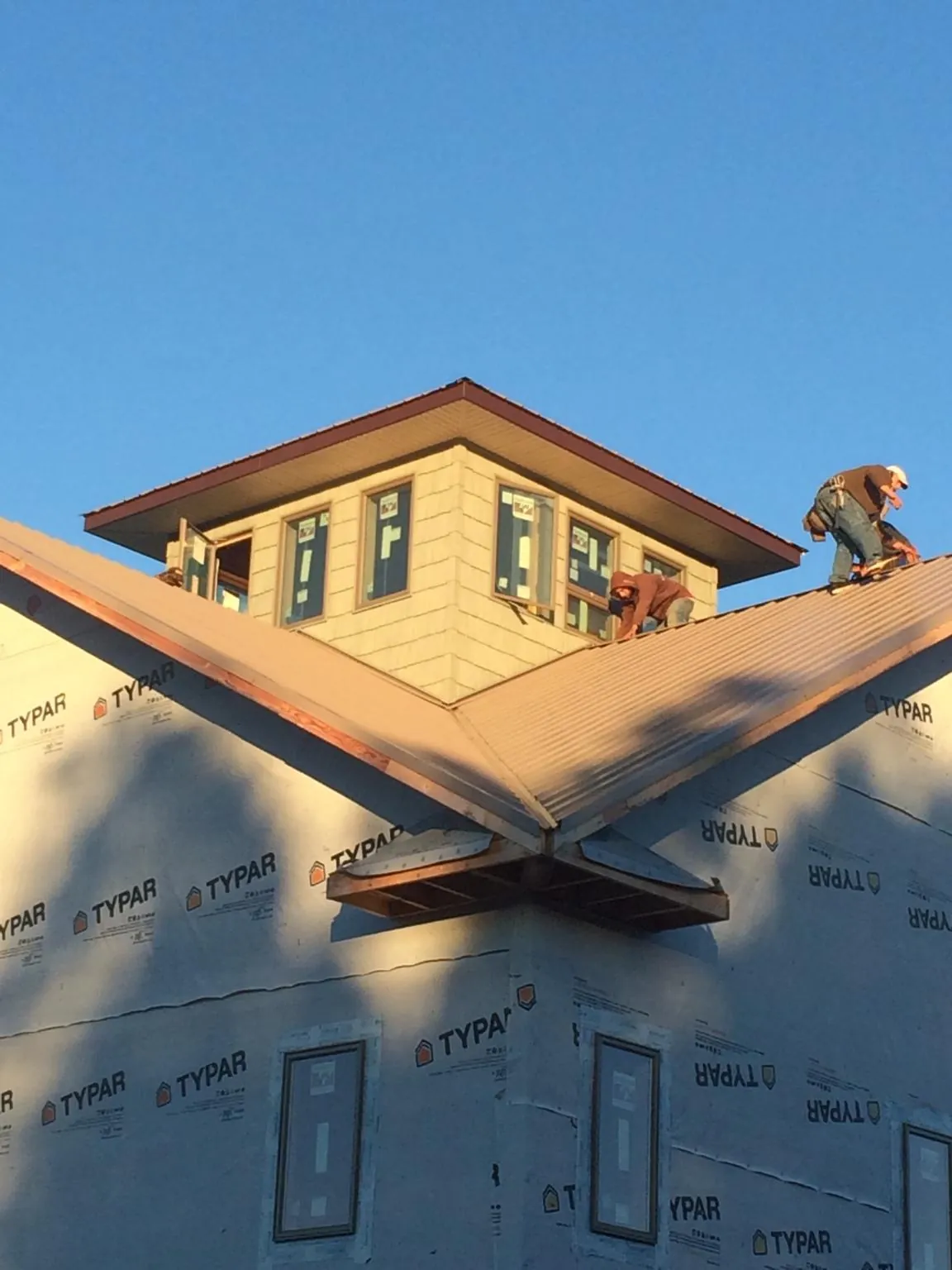 Roofers working around a rooftop cupola on a new metal roof at sunset — Roof Waterproofing in Ellenburg Center by Roofing Brothers